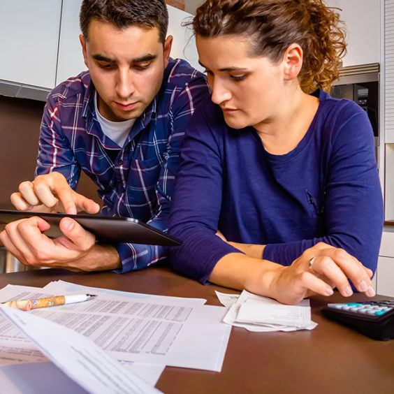 Young couple reviewing their bank accounts with a digital tablet and calculator at home.