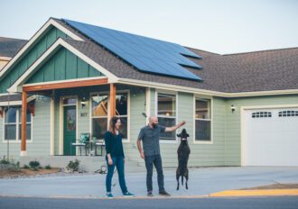 Man and woman walking in front of their house while their dog is doing a trick.