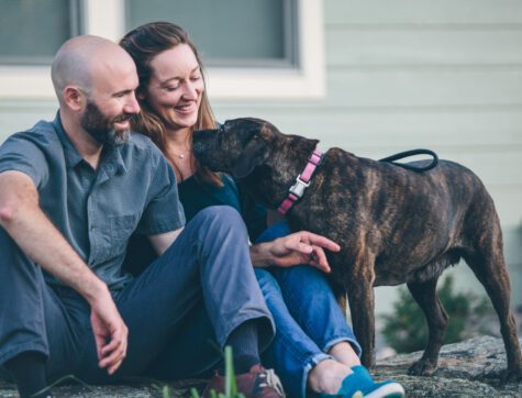 Man and woman sitting the front steps to their house with their dog.