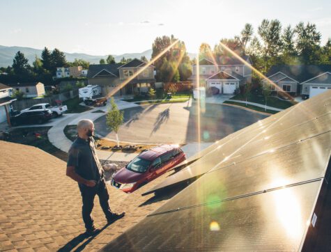 Man standing on top of his roof next to his solar panels during sunset.