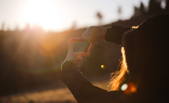 Woman framing the sunset like a picture frame with her hands.