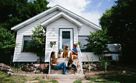 Two women and a dog sitting of the front steps to a white house in Missoula, MT