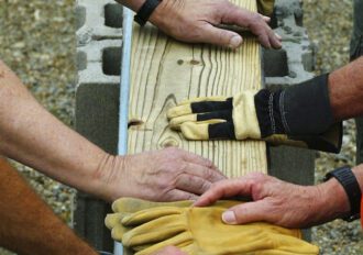 Builders' hands setting a wooden beam in place at a construction site