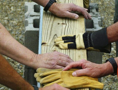 Builders' hands setting a wooden beam in place at a construction site