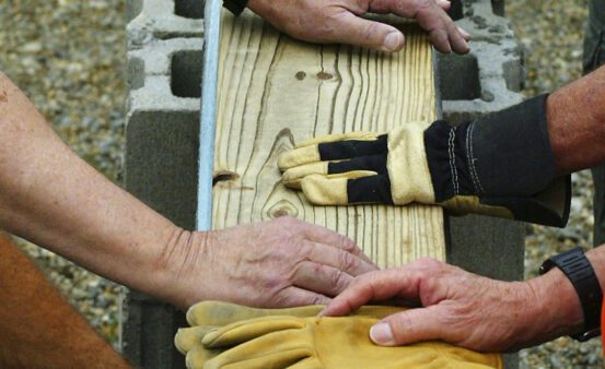 Builders' hands setting a wooden beam in place at a construction site