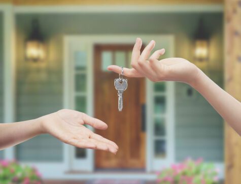 A woman's hand giving a house key to another person's hand.