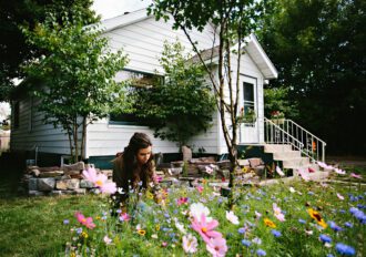 Woman in her front yard planting a garden with her new house in the background.