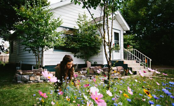 Woman in her front yard planting a garden with her new house in the background.