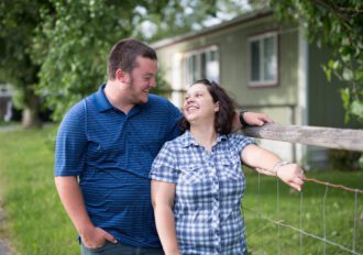 Man and woman standing by the fence outside their nee mobile home.