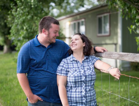 Man and woman standing by the fence outside their nee mobile home.