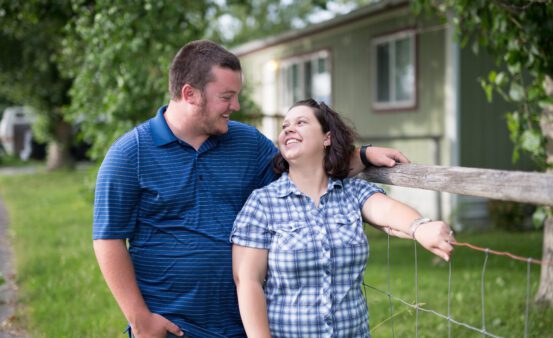 Man and woman standing by the fence outside their nee mobile home.