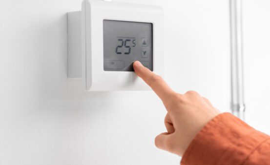 close up of hand setting room temperature on thermostat at home