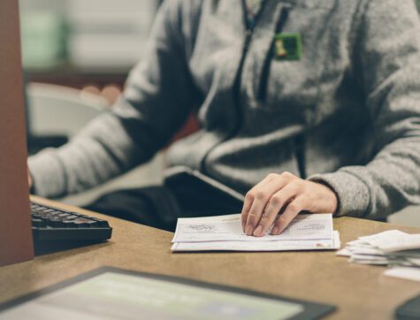 Close up of a man's hand holding a check at a teller counter.