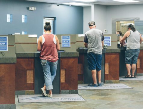 Three Customers standing at 3 teller line stations inside a credit union branch.