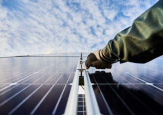 Close up of male worker hand in glove installing photovoltaic solar panel with beautiful cloudy sky on background.