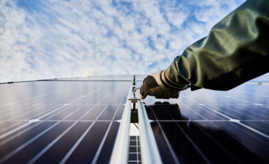 Close up of male worker hand in glove installing photovoltaic solar panel with beautiful cloudy sky on background.