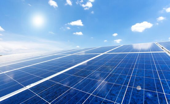 Close-up photo of solar panels with blue sky and white clouds above them.