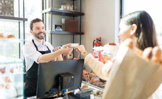 Happy salesman receiving credit card from customer in bakery