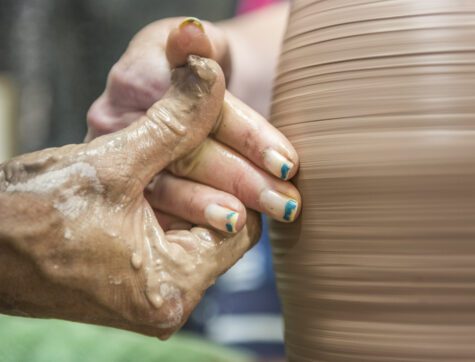 Two hands throwing a clay pot on a pottery wheel.