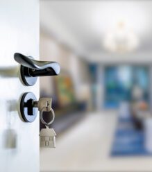 Close-up of keys in door lock with the door partially open to reveal the inside of the house.