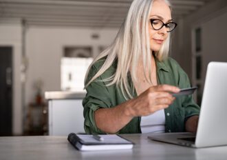 Mature woman using credit card making online payment at home.