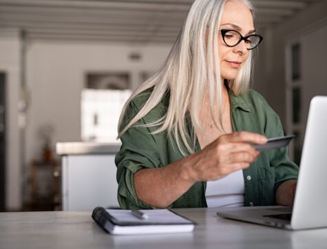 Mature woman using credit card making online payment at home.