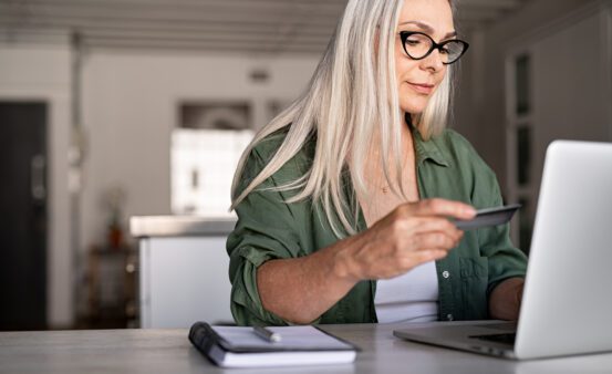 Mature woman using credit card making online payment at home.