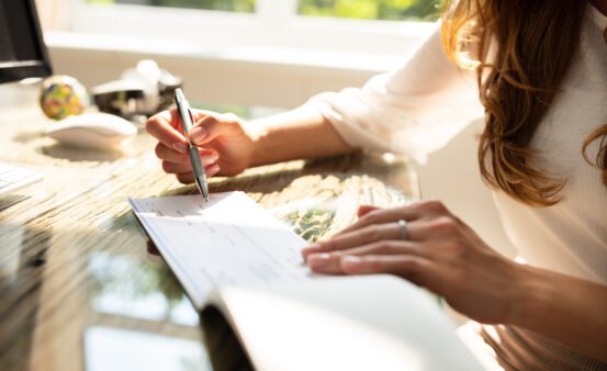 Businesswoman's Hand Signing Check On Wooden Desk