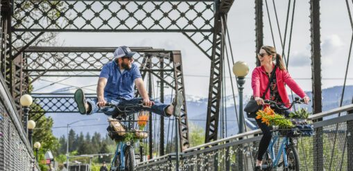 Man and woman riding bicycles across a foot bridge in Missoula Montana on a summer morning.