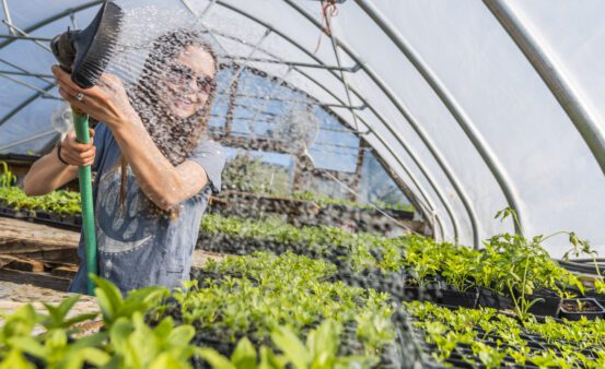 Happy young woman watering plants in a plant nursery.