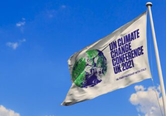 Photo of a UN Climate Change Conference 2021 flag waving against a blue sky.