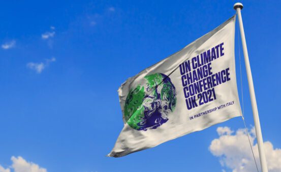 Photo of a UN Climate Change Conference 2021 flag waving against a blue sky.