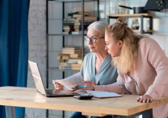 Senior woman using laptop for websurfing in her kitchen. middle-aged daughter helps her mother with documents. Mature lady sitting at work typing a notebook computer in an home office