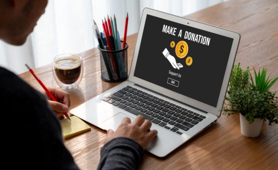 Person sitting at table using a laptop with a donation website on the screen.