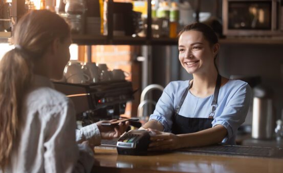 Female customer holding phone near nfc terminal make contactless mobile payment with smiling waitress.