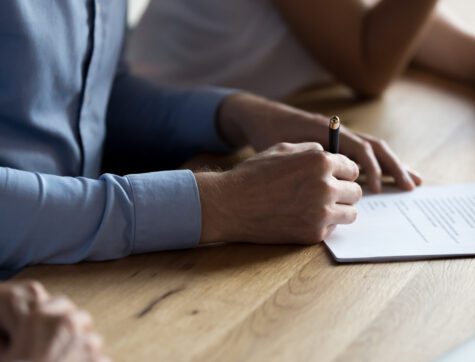 Close up of man hand holding ballpoint and signing legal document.