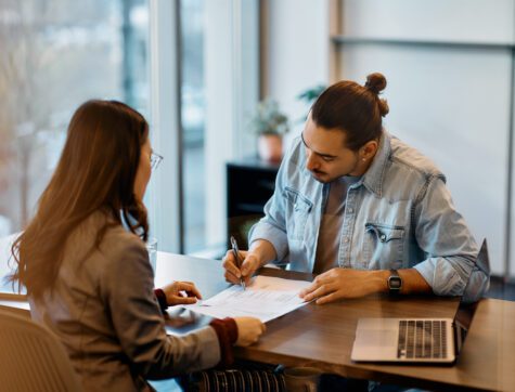 Young man signing documents in a female bankers office.