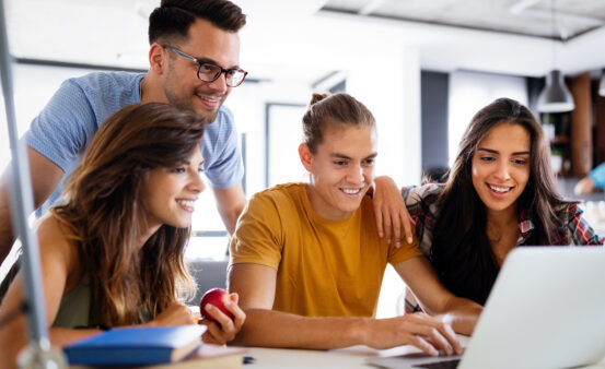 Students surrounding a laptop, looking excited and hopeful