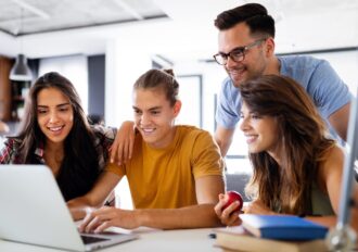 Students surrounding a laptop, looking excited and hopeful