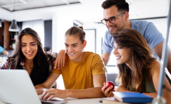 Students surrounding a laptop, looking excited and hopeful