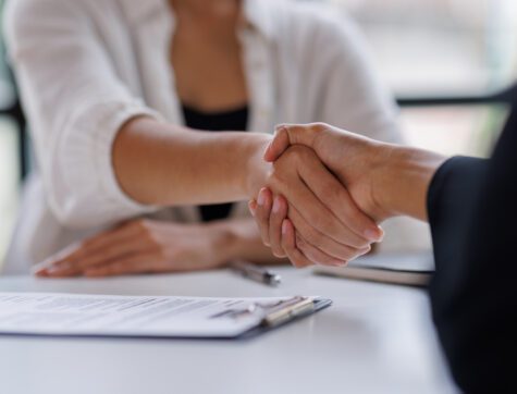 two people shaking hands paperwork nearby