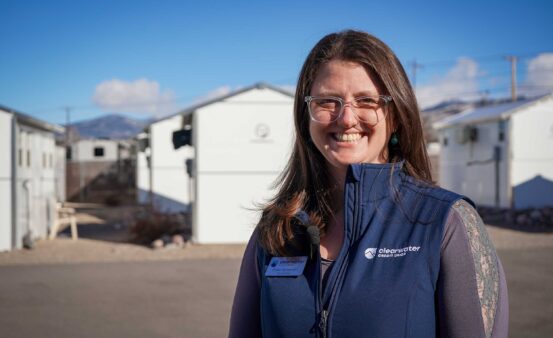 A woman wit brown hair and glasses in a blue vest smiles