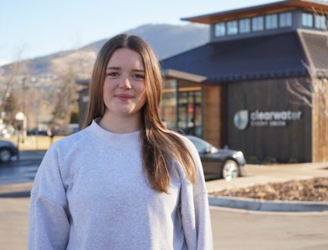 A girl in white sweatshirt stands in front of a Clearwater Credit Union building.