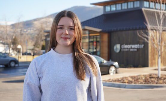 A girl in white sweatshirt stands in front of a Clearwater Credit Union building.