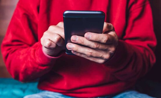 A boy in a red sweatshirt looking at a phone